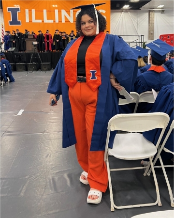 Mya posing in her blue cap & gown, orange hood, and matching slacks